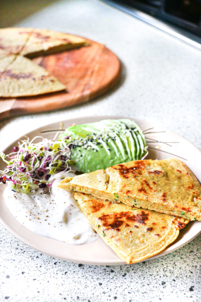 Zucchini breakfast flatbread on a plate with sliced avocado and mayonnaise